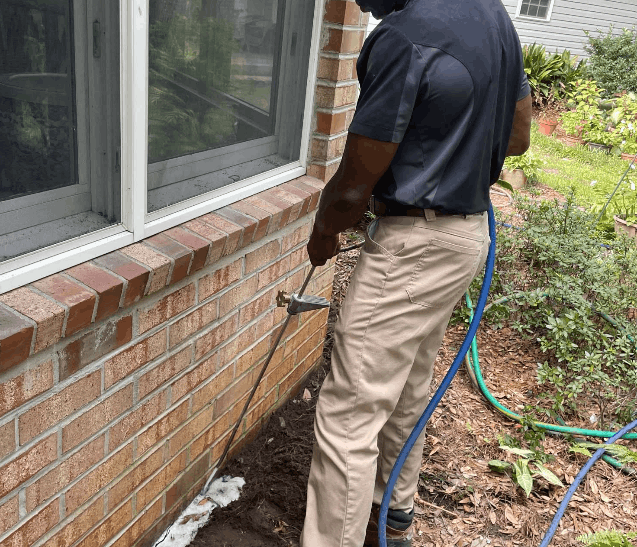 technician spraying for ants along with wall of greensboro home